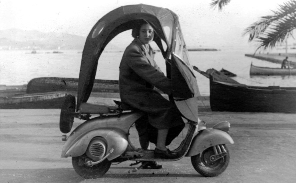 Una donna alla guida di una Vespa con parabrezza e parapioggia, 1948